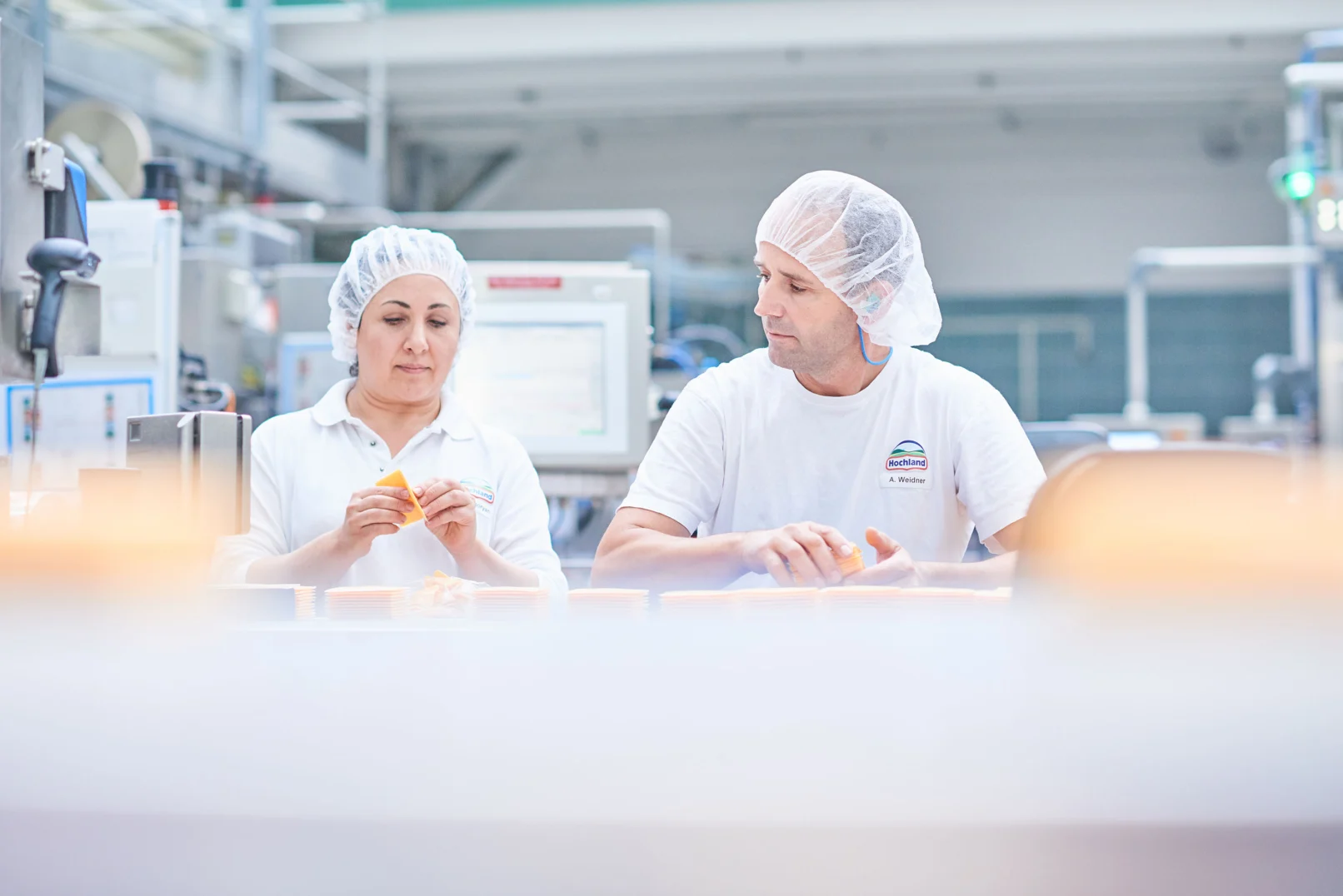 Zwei Mitarbeitende bei der Qualitätskontrolle in der Käseproduktion von Hochland