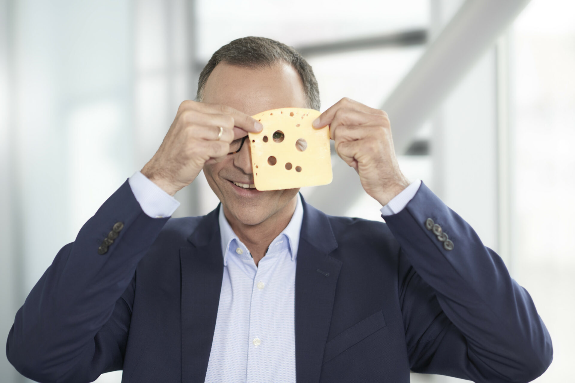 Hochland-Führungskraft hält eine Käsescheibe spielerisch vor das Gesicht
