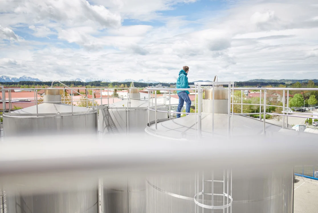 Hochland-Mitarbeiter auf Milchtanks vor dem Alpenpanorama