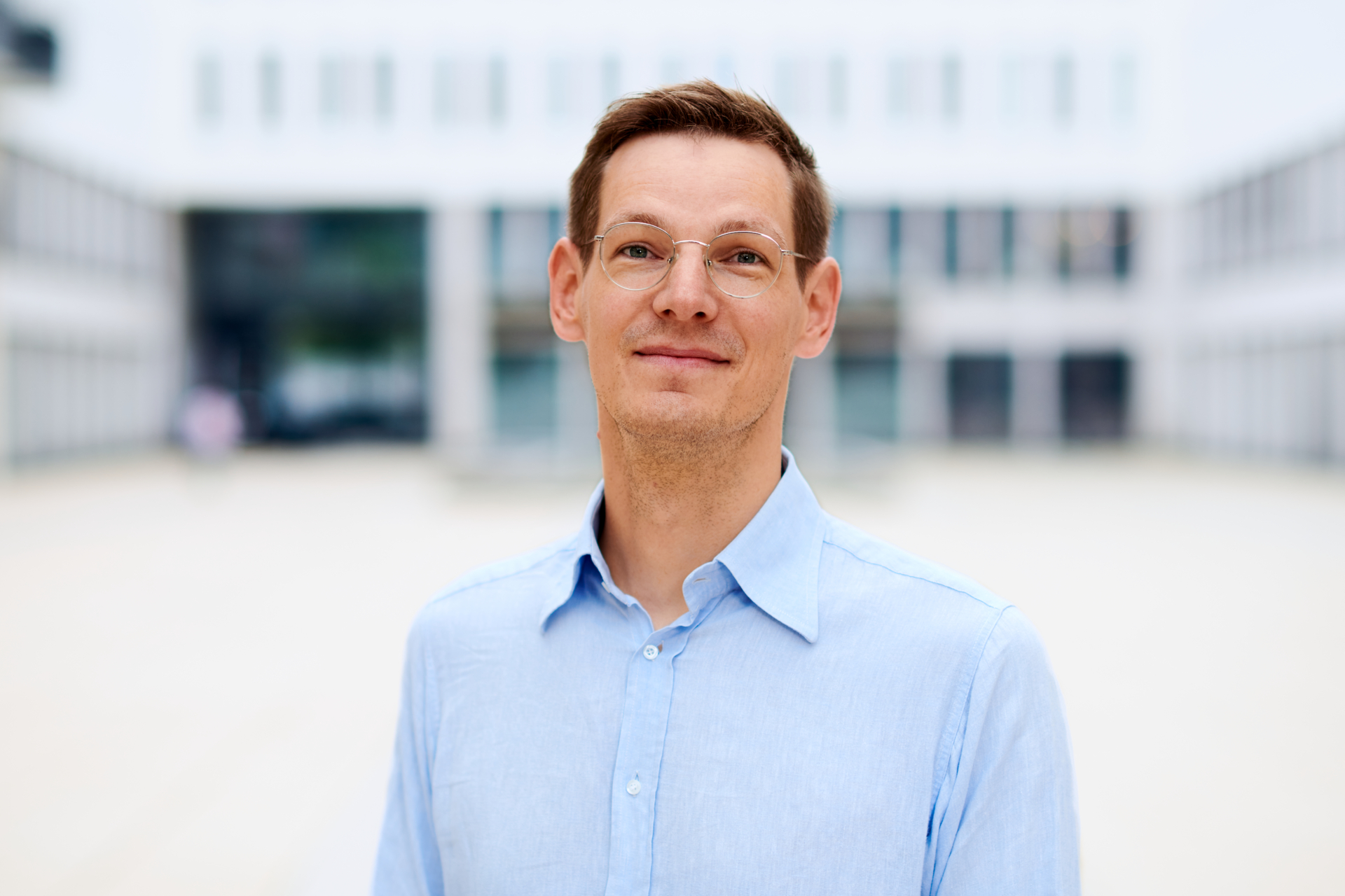 David Klötzer im hellblauen Hemd vor moderner Bürofassade