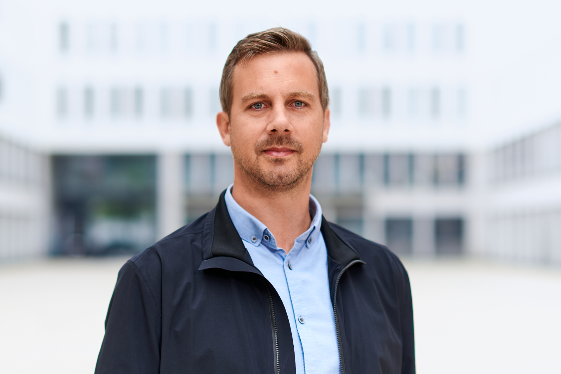 Peter Schindlmeier im offenen Hemdkragen vor moderner Bürofassade