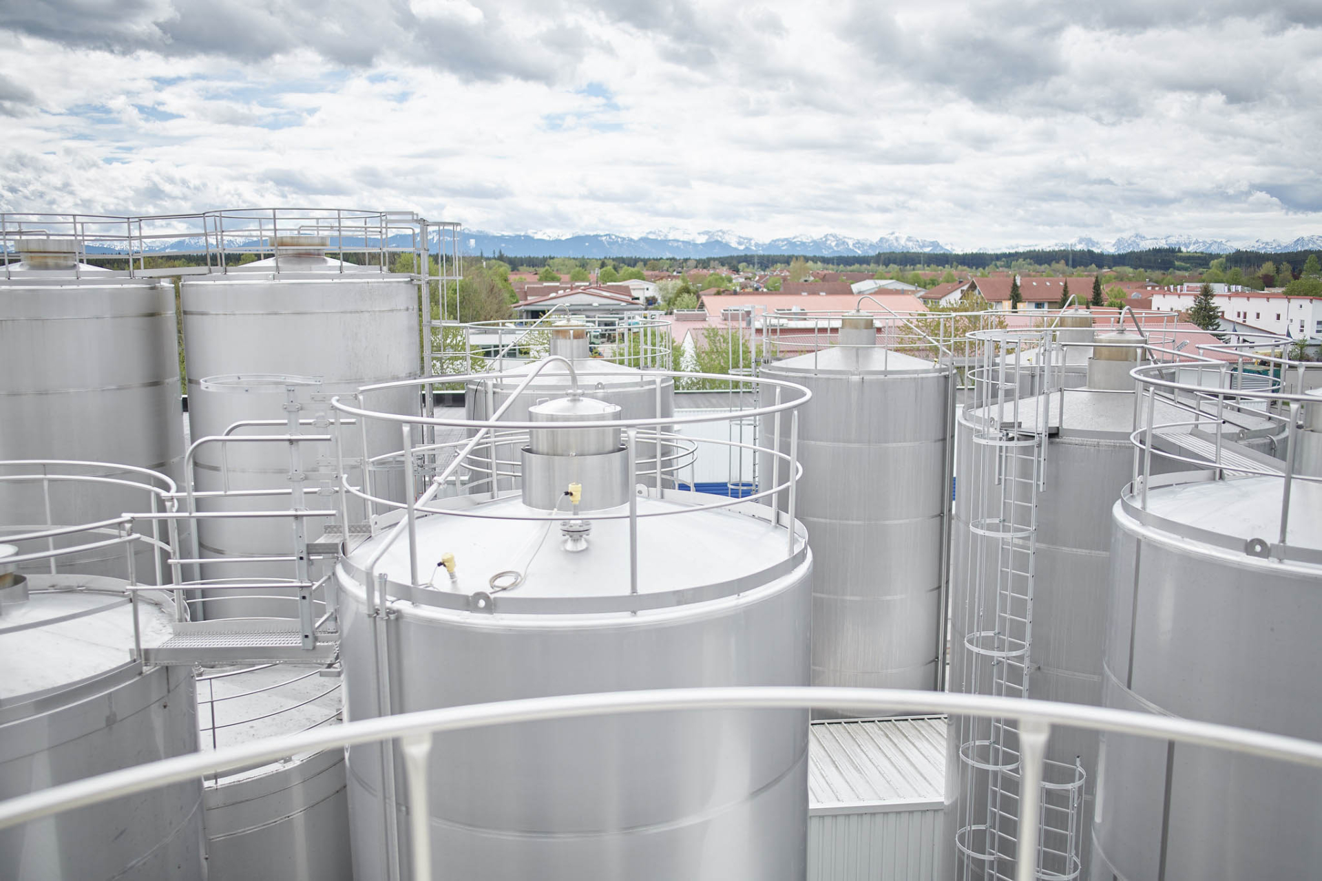 Edelstahltanks am Hochland-Produktionsstandort mit Blick auf Ortschaft und Allgäuer Alpen